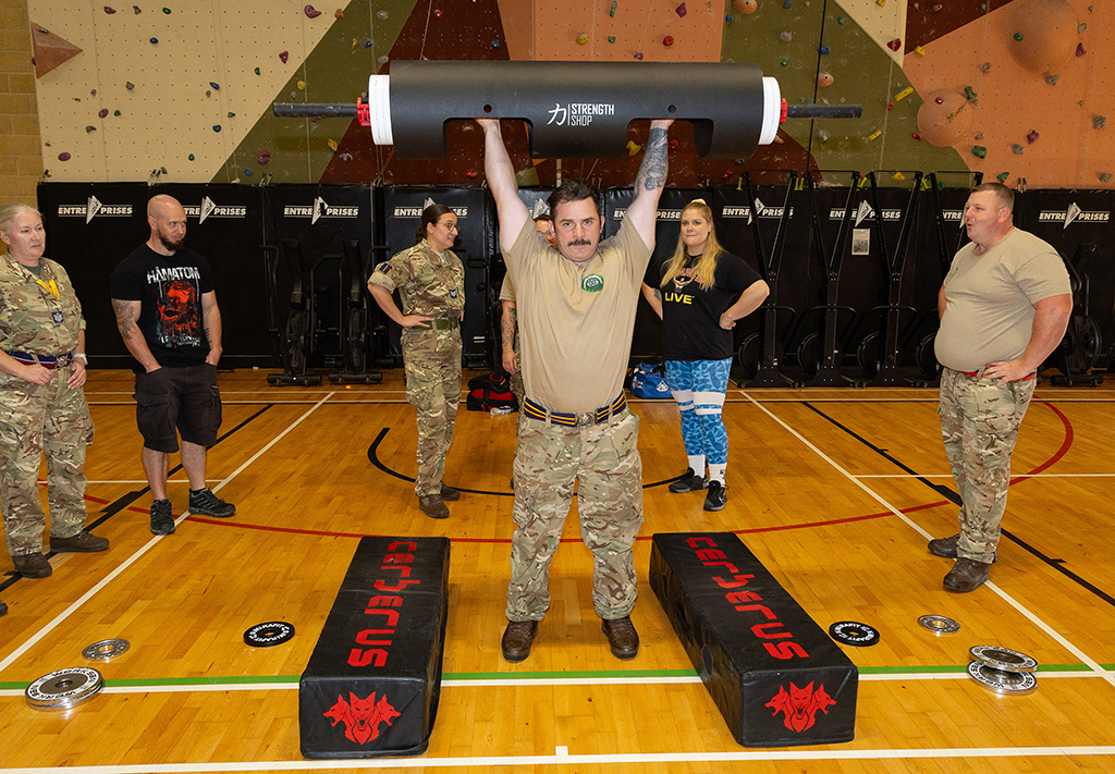 Military personnel watch a demonstration of a weight lifting challenge.
